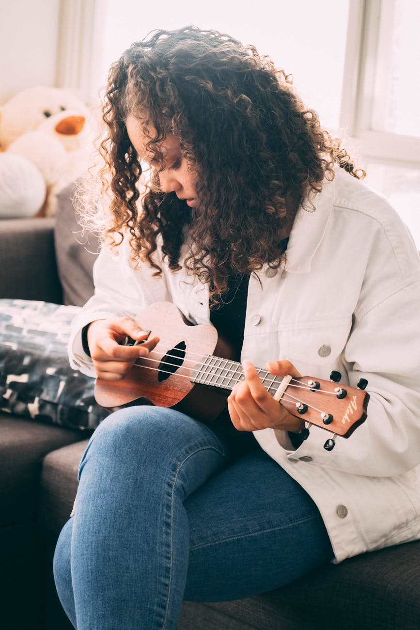 photo of woman playing ukulele white sitting on gray sofa
