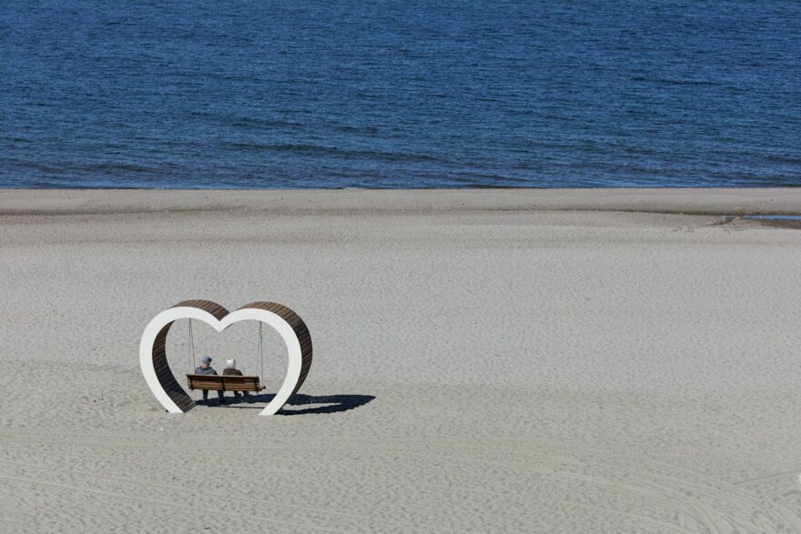 elderly couple seated on bench by sea