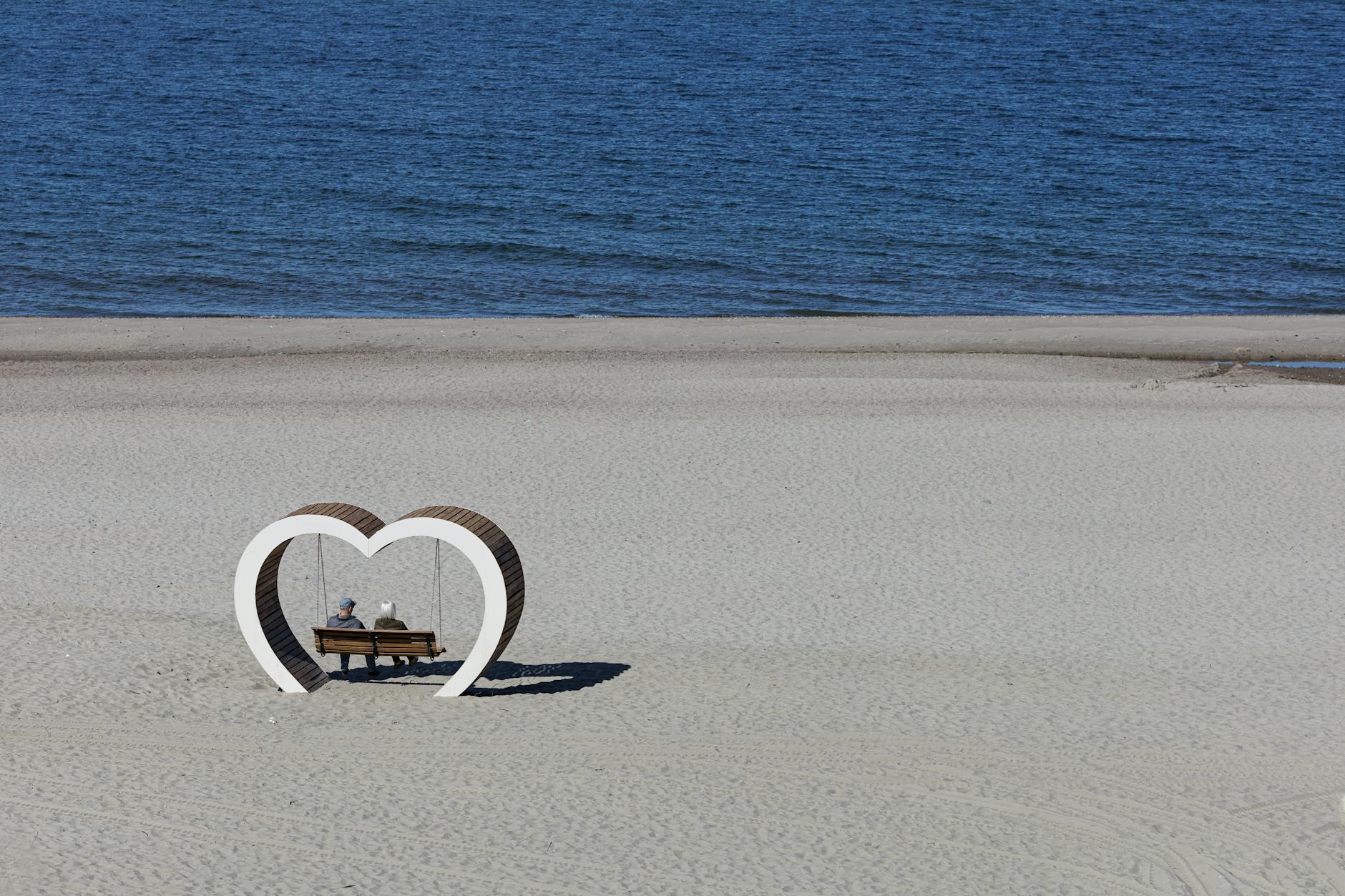 elderly couple seated on bench by sea