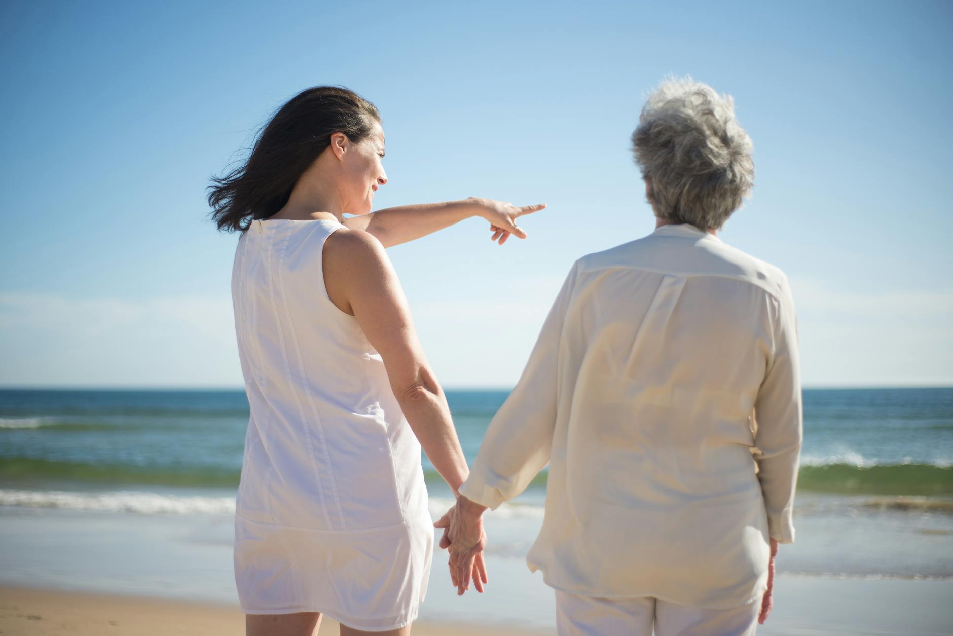woman pointing at the sea while holding the hand of an elderly woman