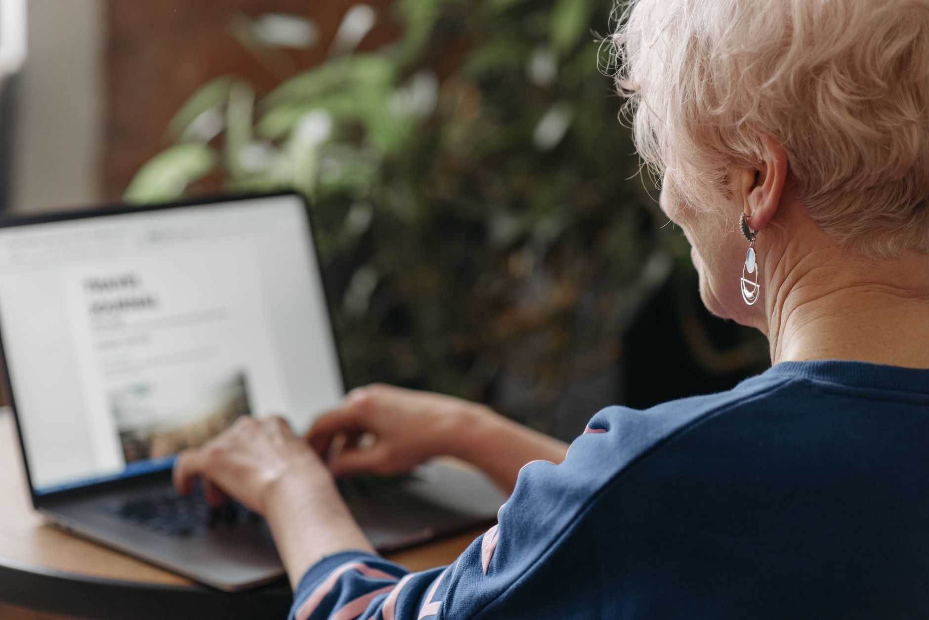 side view shot of woman in blue sweater typing on the keyboard of a laptop